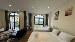A hotel room with two beds, a sofa, a small table, and a large window. - Beachside Bliss Homestay (Phu Quoc)