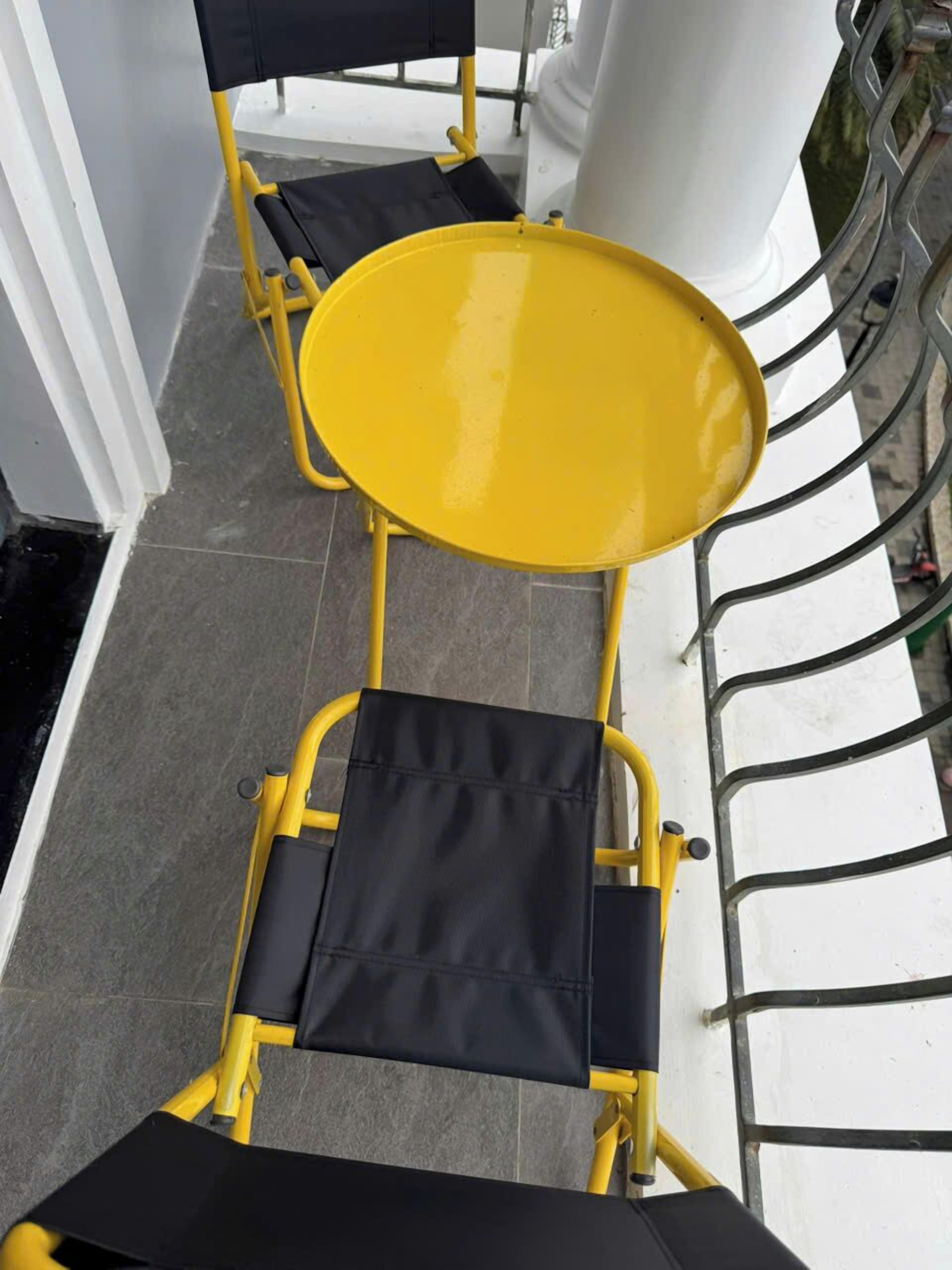 A yellow outdoor table and chair set on a balcony with a white railing.