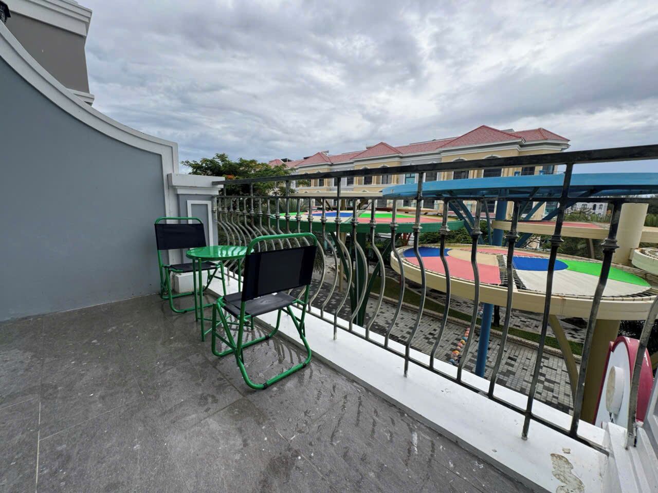 A balcony with a view of a playground and a building with a red roof.