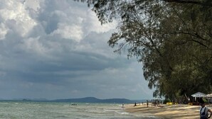 A beach with a sandy shore, a few people, and a cloudy sky. - Beachside Bliss Homestay (Phu Quoc)