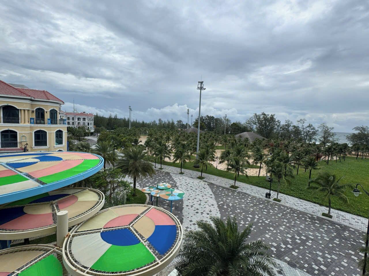 Un parque infantil con zonas de juego circulares y coloridas, y un sendero bordeado de palmeras.