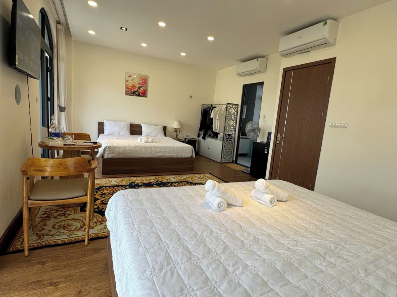 A hotel room with two beds, a desk, a chair, an air conditioner, and a TV.