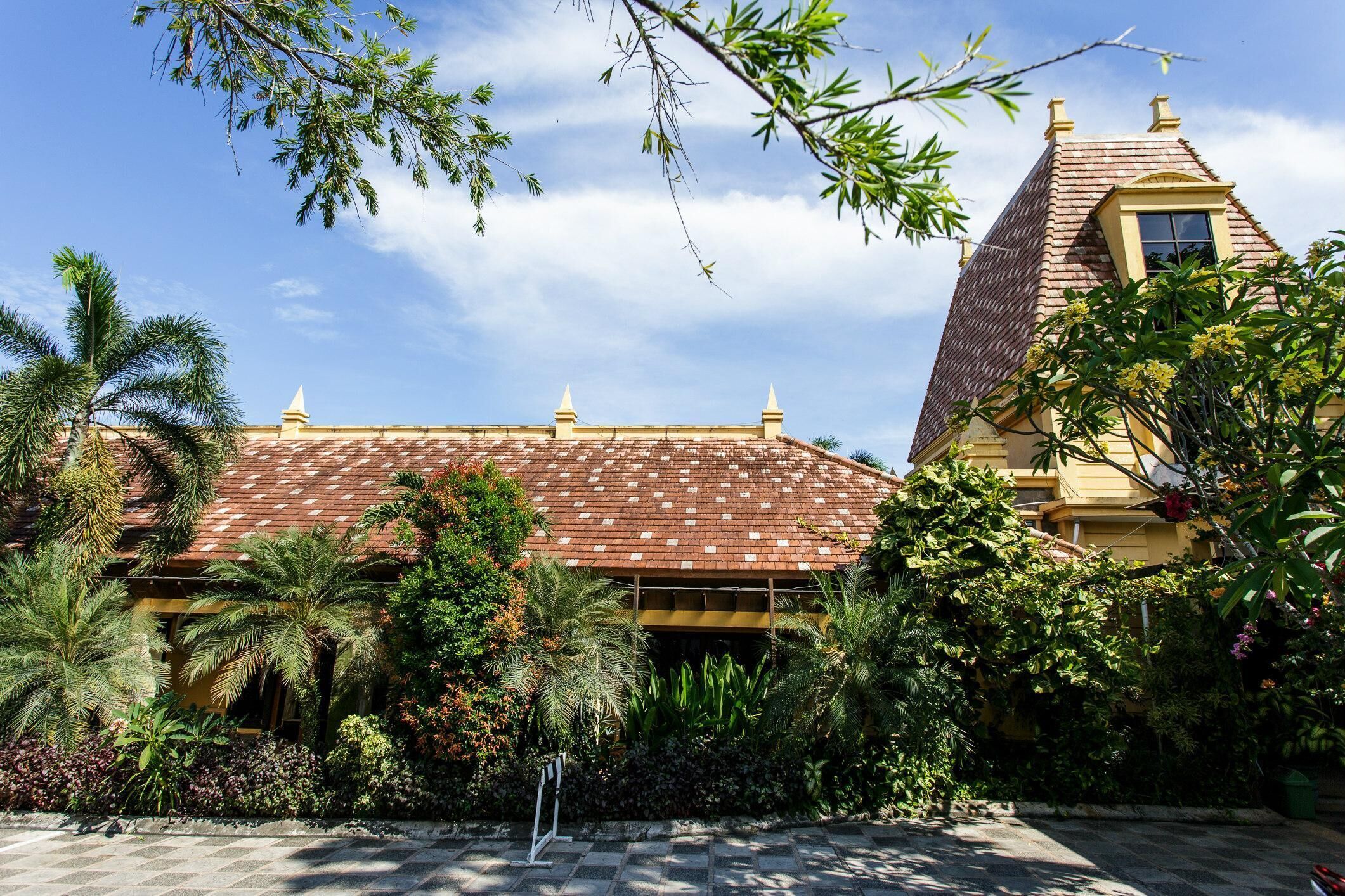 Un bâtiment doté d’un toit en tuiles, entouré d’une végétation luxuriante et de palmiers.