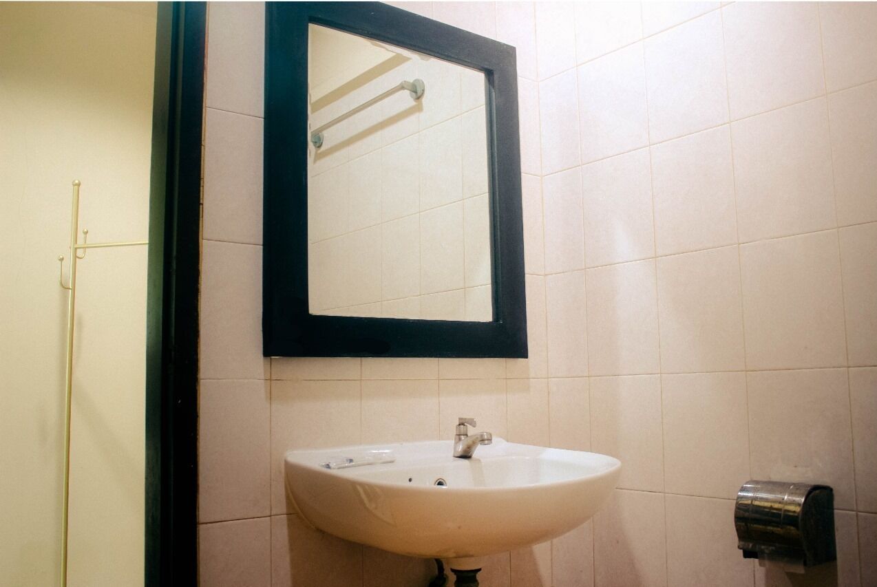 Un baño con un lavabo blanco, un espejo con marco negro y un dispensador de papel higiénico.