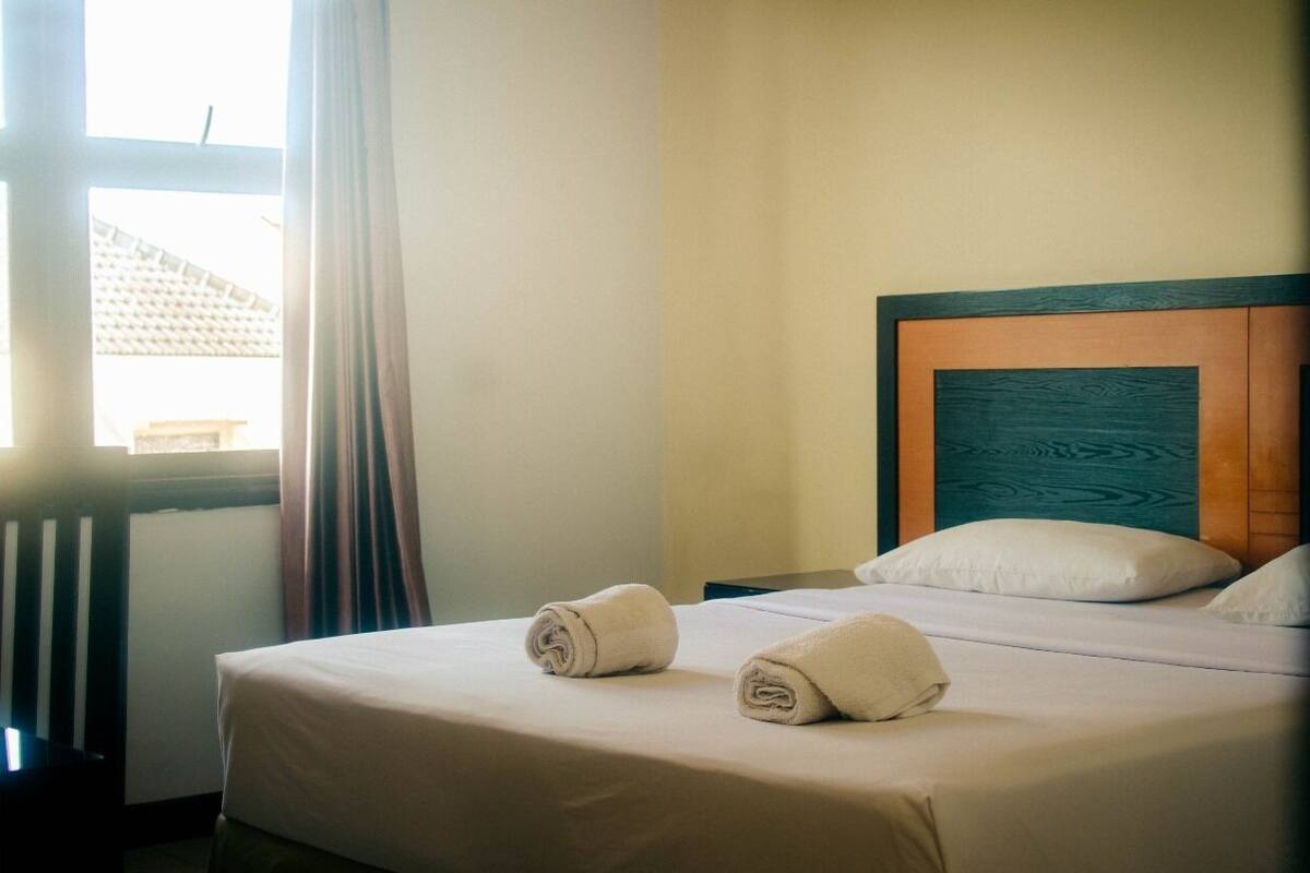 Una camera d'hotel con un letto rifatto, una testiera in legno e una finestra con tende.
