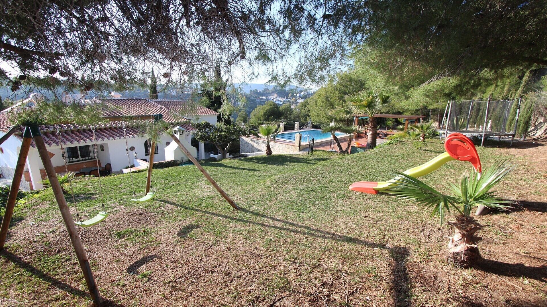 A backyard with a swing set, a pool, and a house with a tiled roof.