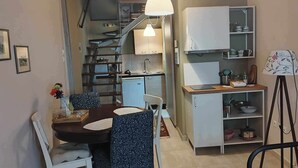A compact kitchen with a dining area, a small refrigerator, and a shelf with kitchenware.