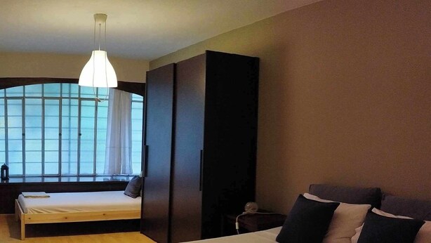 A bedroom with a bed, a wardrobe, a desk, and a window with curtains.