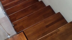 A wooden staircase with a handrail, a small window with a red light, and a framed picture on the wall.