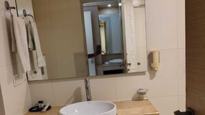 Une salle de bain avec un lavabo blanc, un miroir, un porte-serviettes et un distributeur de savon.