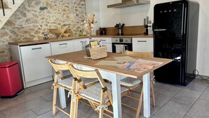 A kitchen with a wooden table, chairs, a refrigerator, and a stone wall.