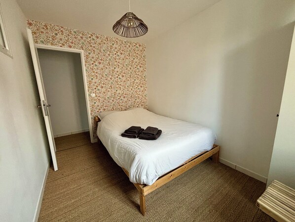 Una habitación pequeña con cama individual, estructura de madera, papel tapiz estampado y una lámpara colgante.