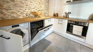 A compact kitchen with a stone wall, built-in dishwasher, oven, and white cabinetry.