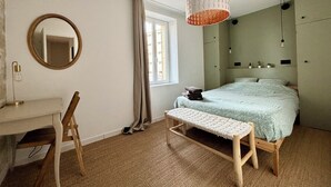 A bedroom with a bed, a desk, a bench, a mirror, and a hanging light fixture.
