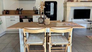 A modern kitchen with a wooden table, two chairs, a vase with dried flowers, and a television above the counter.