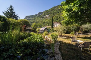 Un jardín con un estanque, sillas y una casa con techo inclinado.