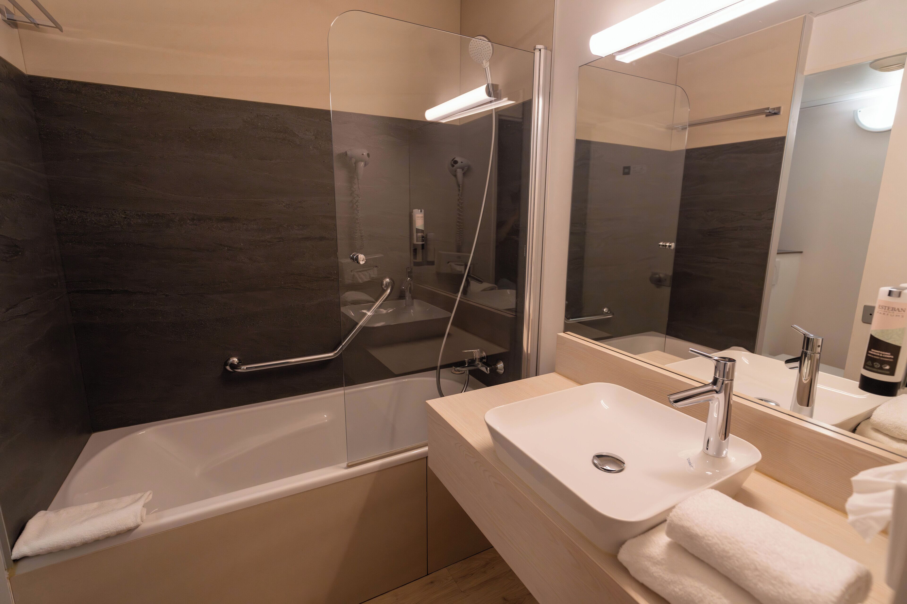 A modern bathroom with a bathtub, a glass-enclosed shower, a sink, and a mirror.