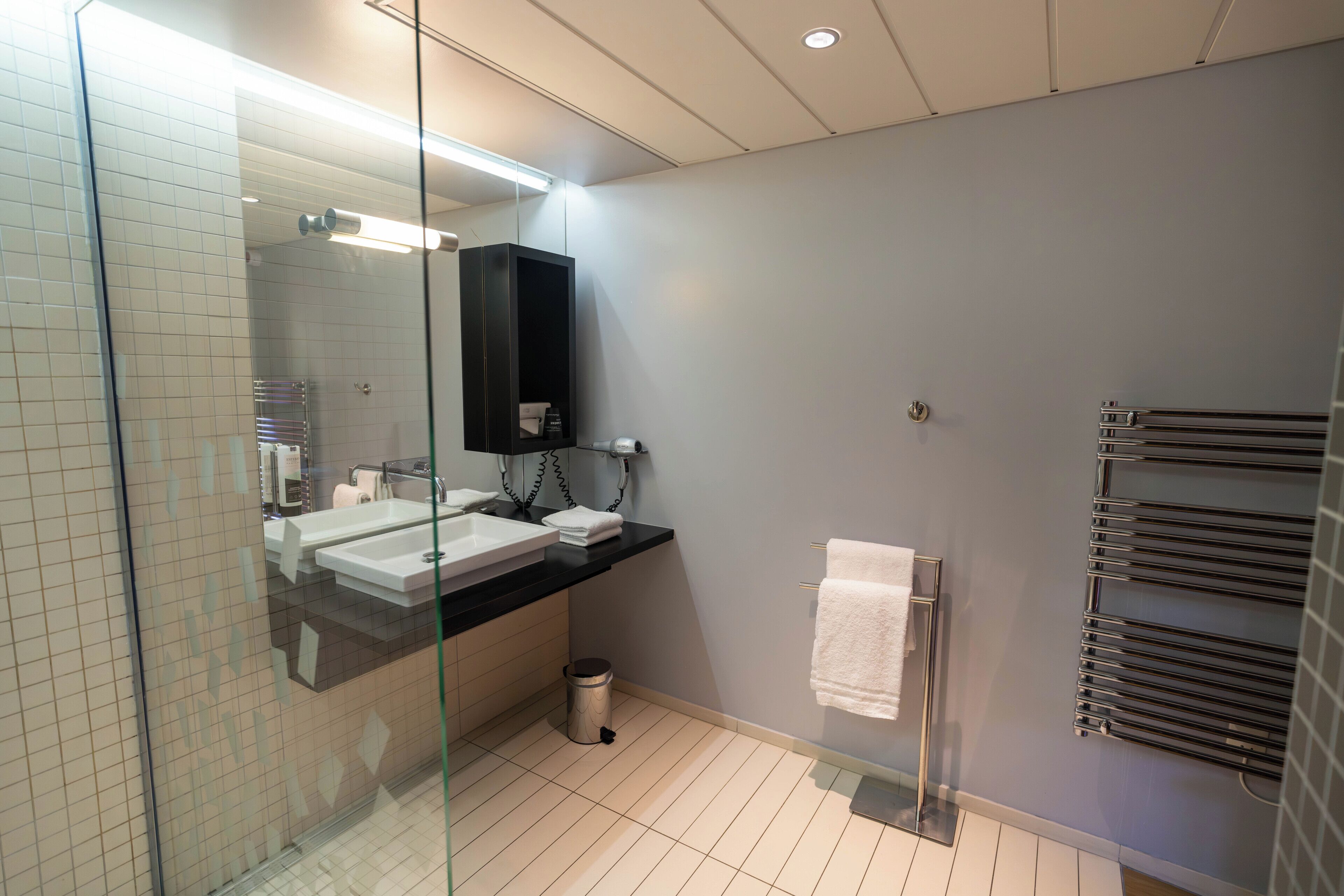A modern bathroom with two sinks, a glass shower enclosure, a towel rack, and a towel hanging on the wall.