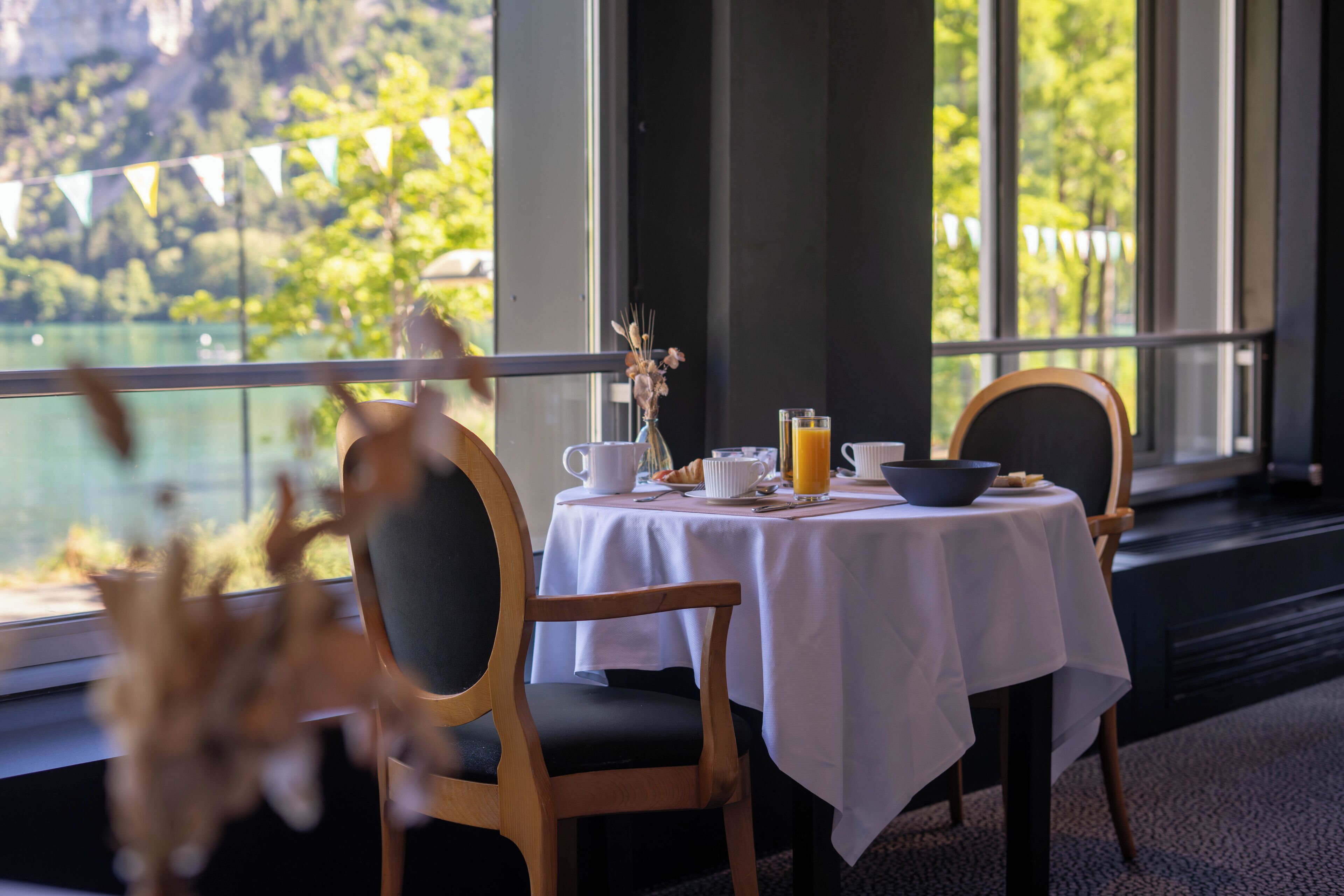 A dining area with a table set for two, a view of a lake, and a balcony with a string of flags.