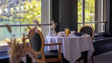 A dining area with a table set for two, a view of a lake, and a balcony with a string of flags.