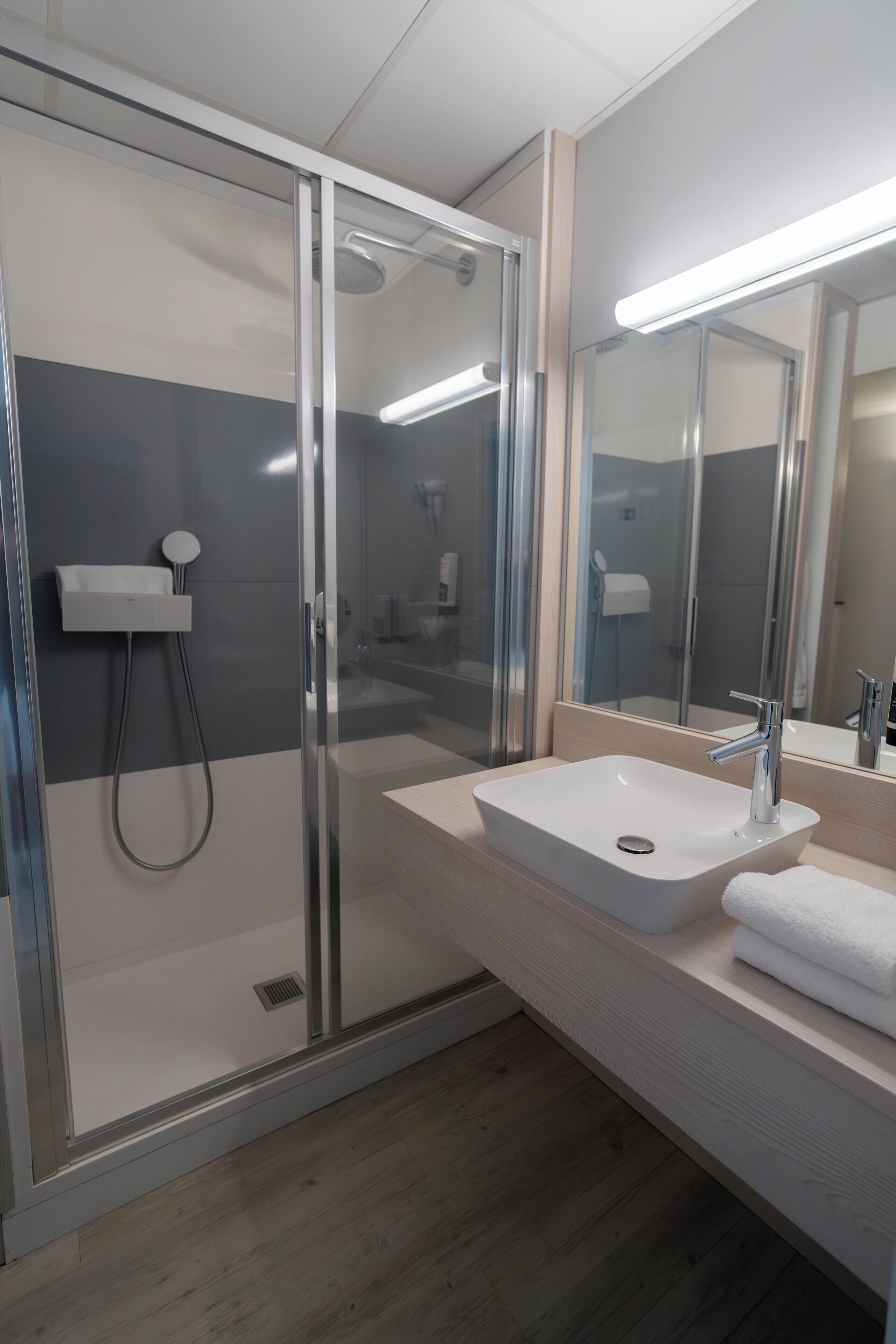 Un bagno moderno con doccia vetrata, lavandino bianco e specchio sopra.