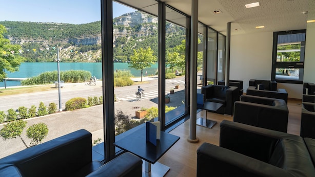A modern interior with large windows offering a view of a lake and mountains. - Logis Hotel L'Embarcadère (Nantua)