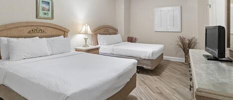 A hotel room with two beds, a TV, a lamp, and a picture on the wall.