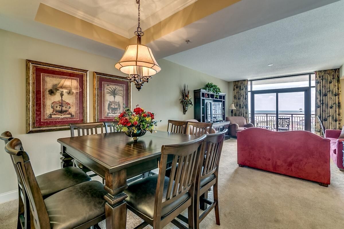 A dining area with a wooden table and chairs, a chandelier, and framed artwork on the wall.