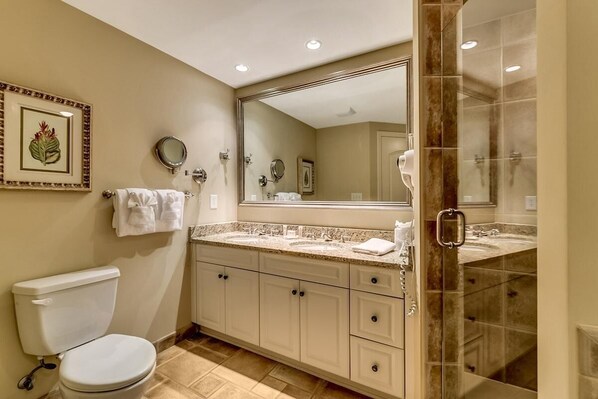 A bathroom with a toilet, a sink, a large mirror, and a shower area.