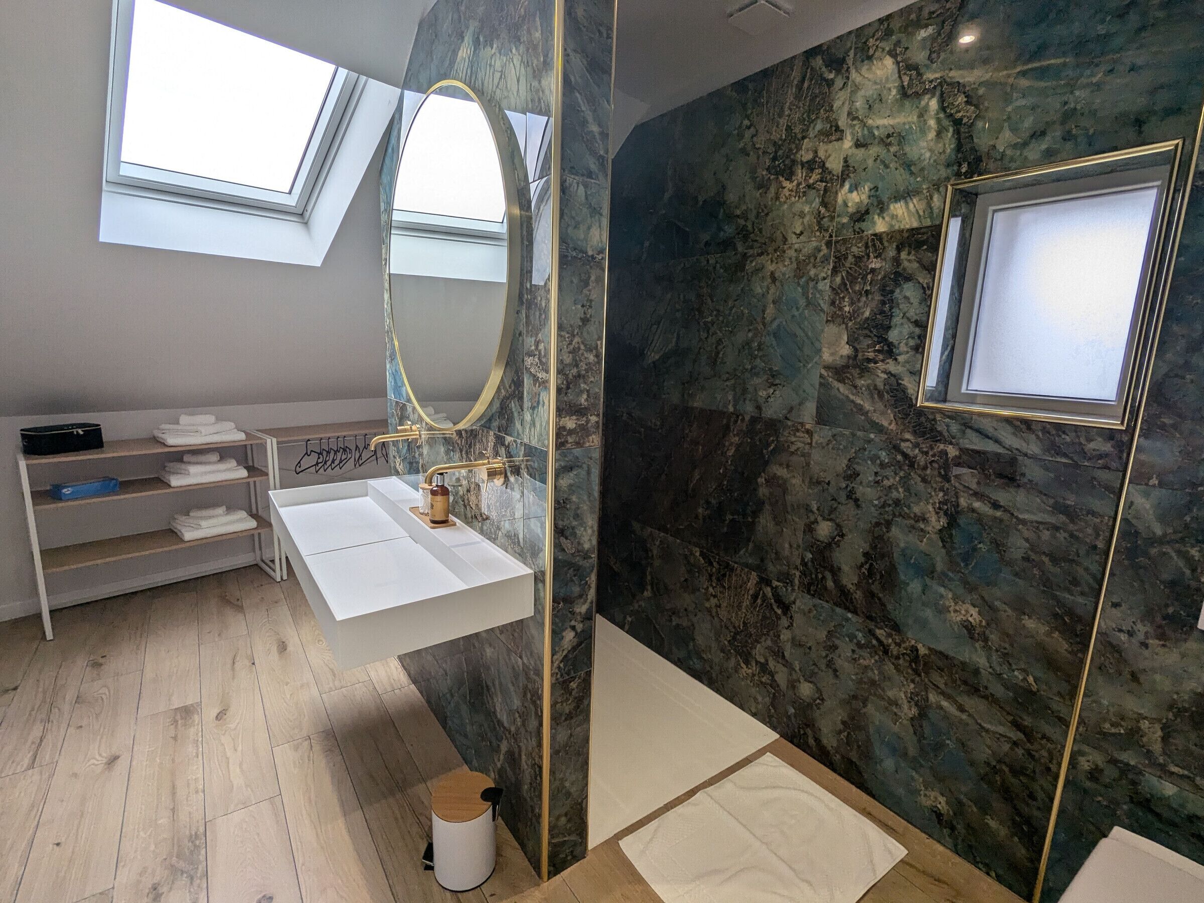 A modern bathroom with a skylight, a white sink, a marble wall, and a large mirror.