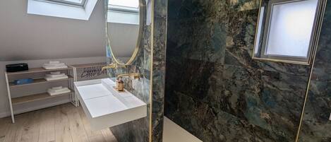 A modern bathroom with a skylight, a white sink, a marble wall, and a large mirror.