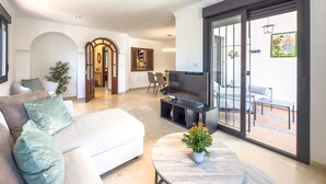 A modern living room with a sofa, a coffee table, and a TV. There is a sliding glass door leading to an outdoor area.
