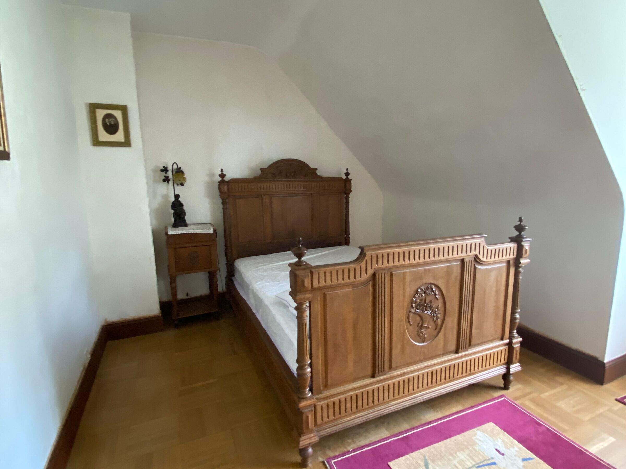 Un dormitorio con una cama con dosel de madera, una mesita de noche y una pequeña mesa con un florero.