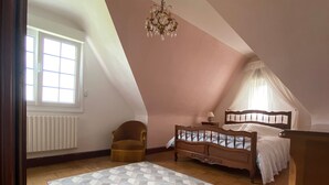 A bedroom with a bed, a chair, a chandelier, and a window.