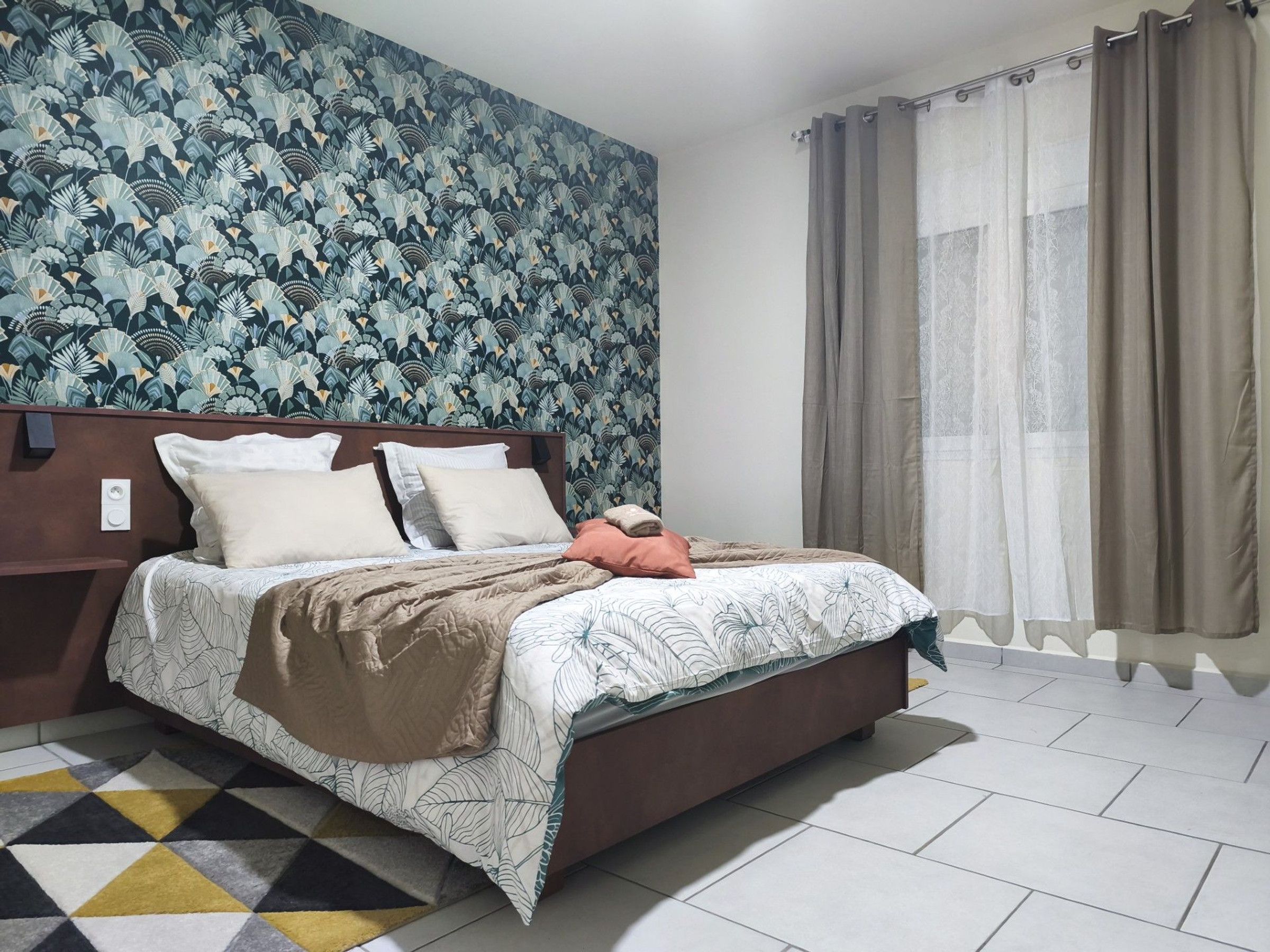 A neatly made bed with a patterned bedspread, a brown headboard, and a geometric rug.