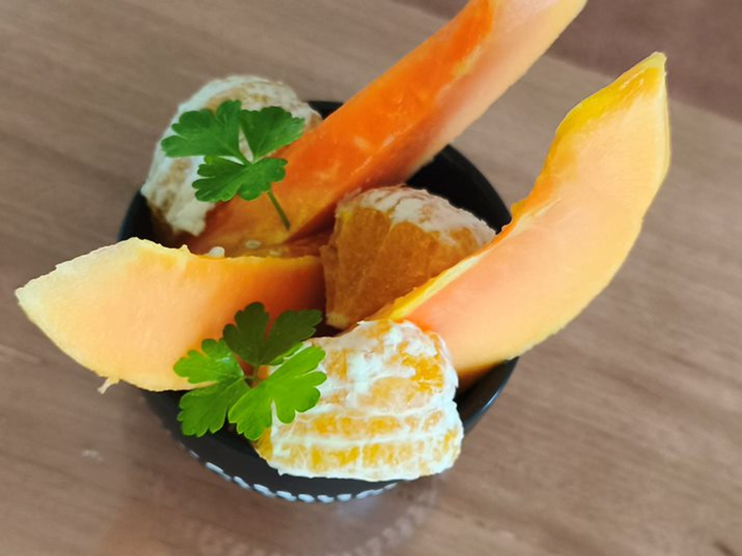 En skål med skiver af cantaloupe melon og appelsinstykker, pyntet med persille.