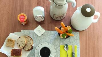 A breakfast setup with a coffee pot, teapot, and teacup, along with bread, butter, jam, and orange slices on a table.
