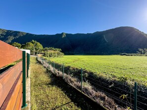 Un campo cercado con una estructura de madera a la izquierda, cielo despejado y una montaña al fondo.