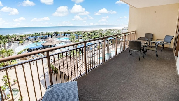 A balcony with a view of a beach and pool area, including lounge chairs and umbrellas.