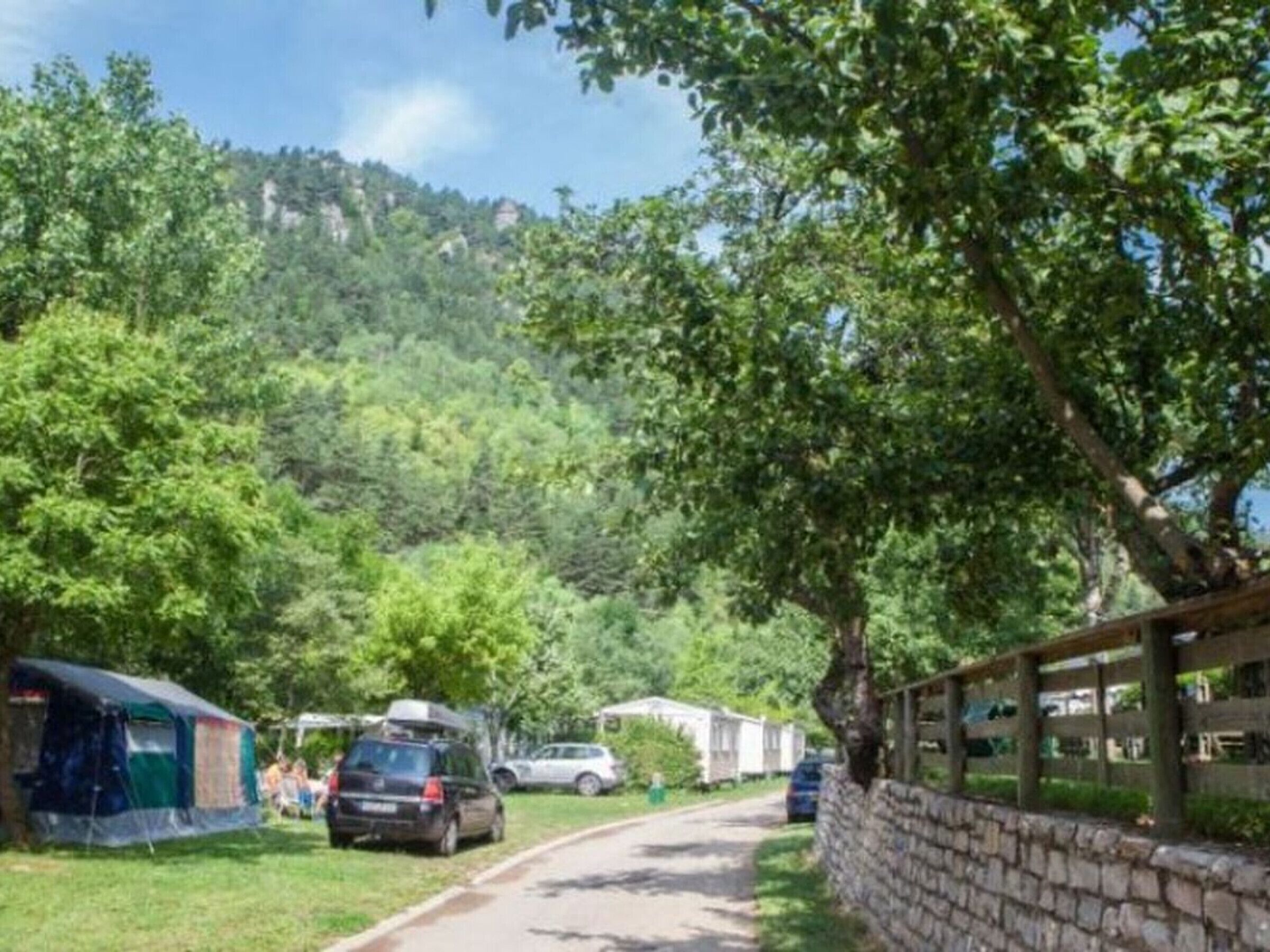 A campsite with tents and RVs parked along a road, surrounded by trees and hills.