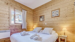 A wooden-paneled room with a bed, a window with curtains, a bedside table with a lamp, and framed pictures on the wall. - Champagny en Vanoise: 3 Rooms for 6 pers. with WIFI and Parking (Champagny-en-Vanoise)