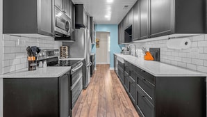 A kitchen with dark cabinets, stainless steel appliances, and a wooden floor.