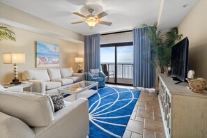 A hotel room with a balcony, a ceiling fan, a TV, and a large window.