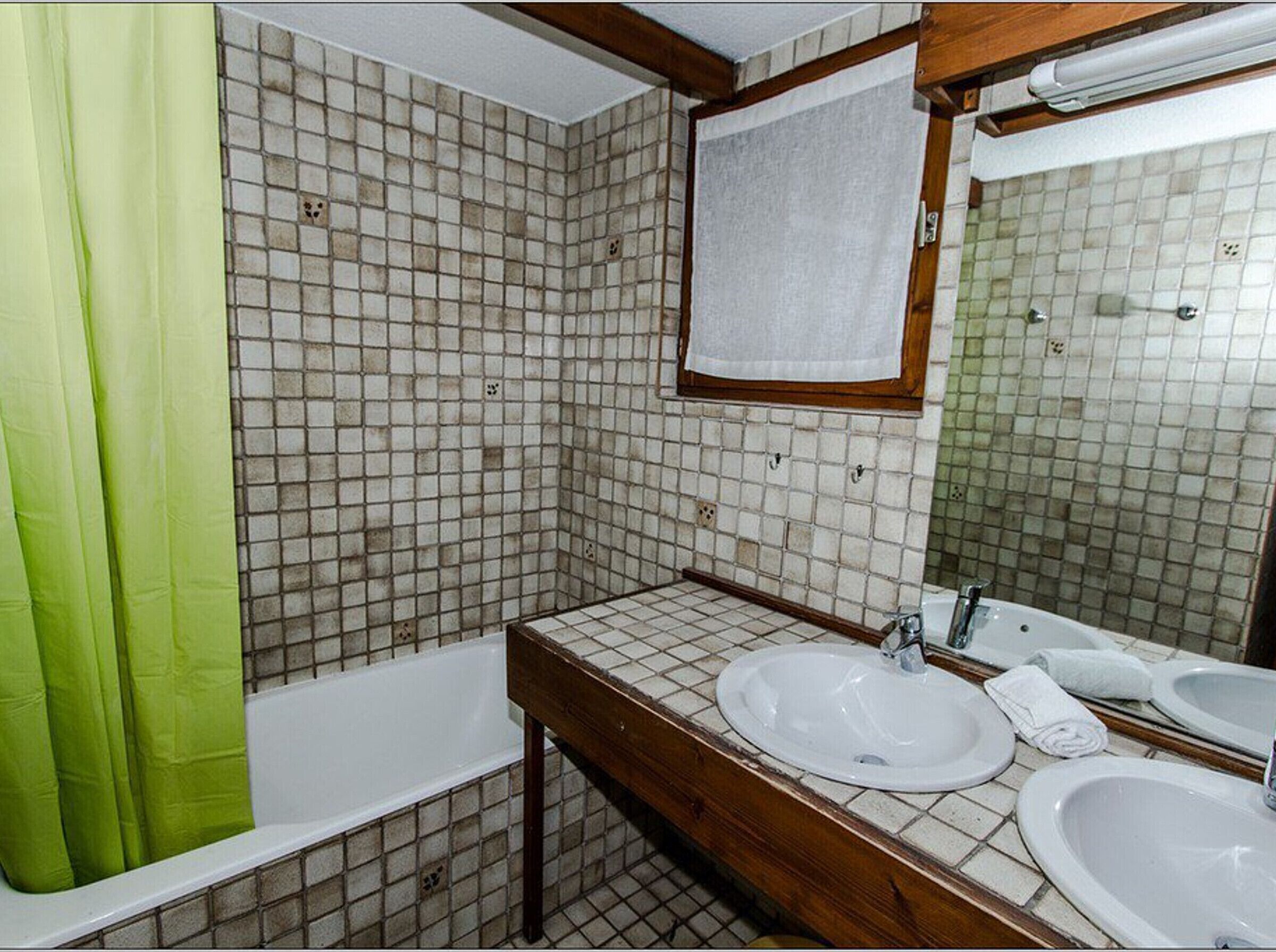 A bathroom with a bathtub, two sinks, a mirror, and a green shower curtain.