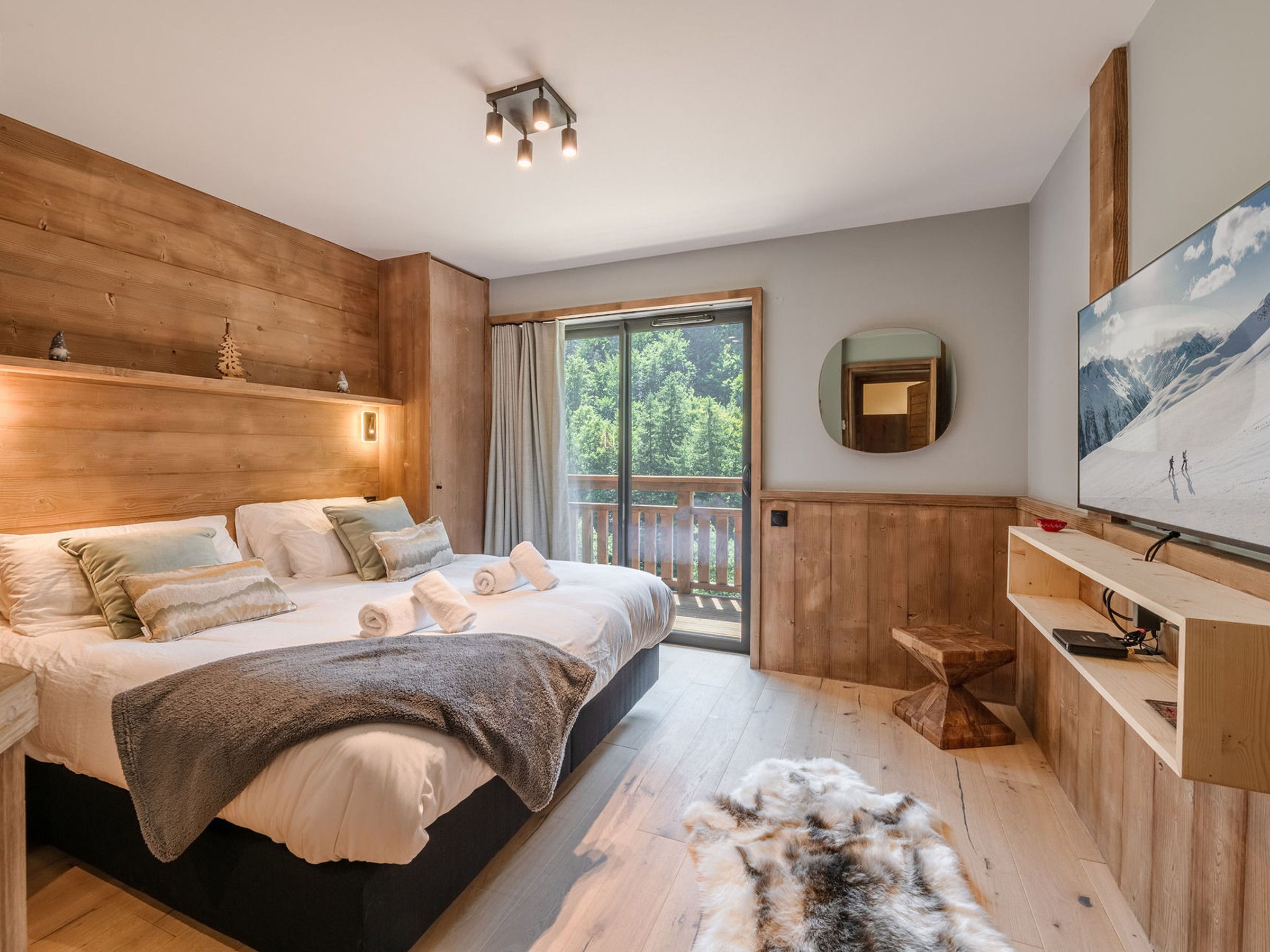 A modern bedroom with a large bed, a wooden headboard, a television, and a view of a snowy mountain through a sliding glass door.