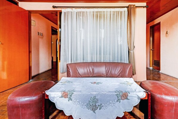 A room with a bed, two red armchairs, a table with a floral tablecloth, and a curtain. - Collection O My Grand (Cisarua)