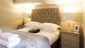 A neatly made bed with a patterned headboard, two bedside lamps, a nightstand with a framed picture, and a pair of folded towels.