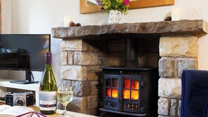 A stone fireplace with a wood-burning stove, a bottle of wine, a glass, and a camera on a table.