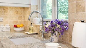 A kitchen with granite countertops, a sink, a coffee maker, a vase with flowers, and a bowl of fruit.