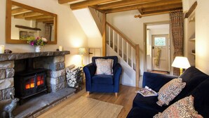 A cozy living room with a stone fireplace, a blue armchair, a dark blue sofa, and a staircase leading upstairs.